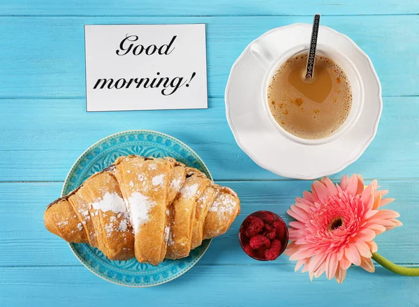 Assiette avec croissant, tasse de café et fleur sur la table, vue sur le dessus. Petit déjeuner savoureux et souhait "Bonjour" — Photo