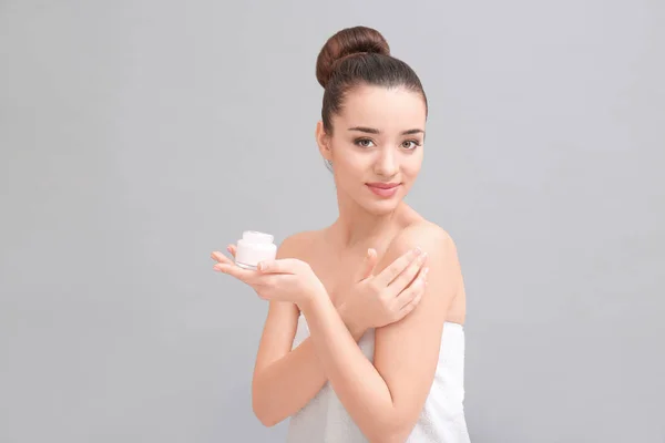 Young woman applying body cream on light background — Stock Photo, Image