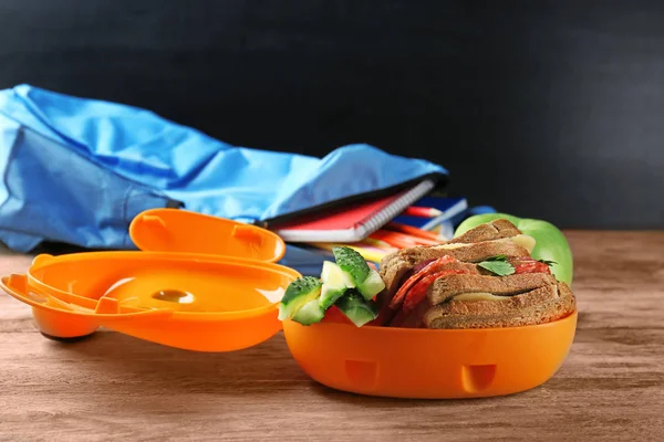 Oběd box s jídlem pro školák a batoh na tmavém pozadí — Stock fotografie