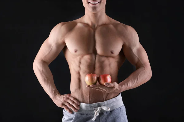Bello muscoloso giovane uomo con mele su sfondo nero — Foto Stock