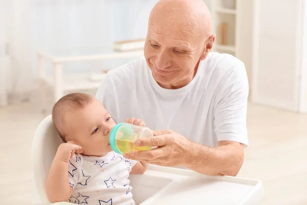 Hombre mayor dando de beber a su nieto en casa —  Fotos de Stock
