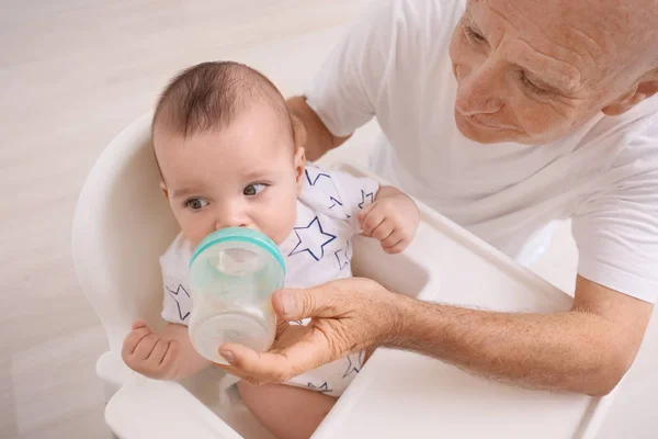 Senior gibt seinem kleinen Enkelkind zu Hause etwas zu trinken — Stockfoto