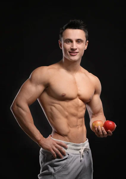 Pohledný svalnatý mladý muž s jablky na černém pozadí — Stock fotografie