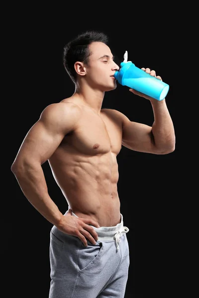 Schöner muskulöser junger Mann trinkt Proteinshake auf schwarzem Hintergrund — Stockfoto