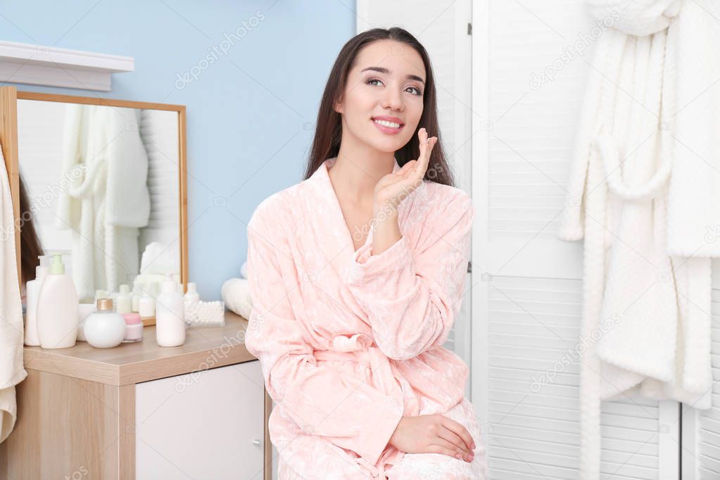 Young woman applying face cream indoors