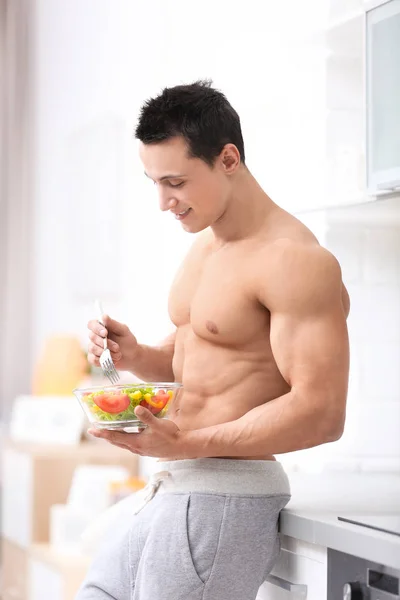 Bonito jovem musculoso comendo salada na cozinha — Fotografia de Stock