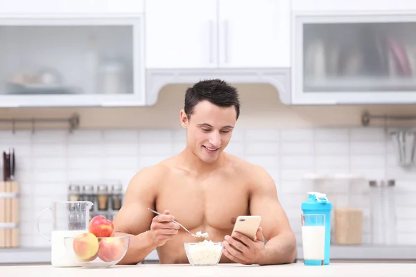 Handsome muscular young man counting calories while having healthy breakfast in kitchen