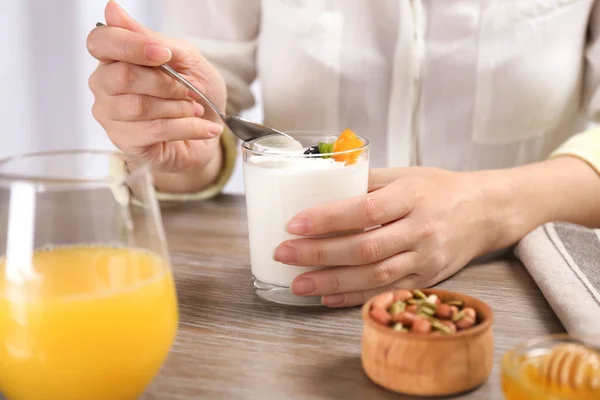 Nainen syö maukasta jogurttia aamiaiseksi pöydässä — kuvapankkivalokuva
