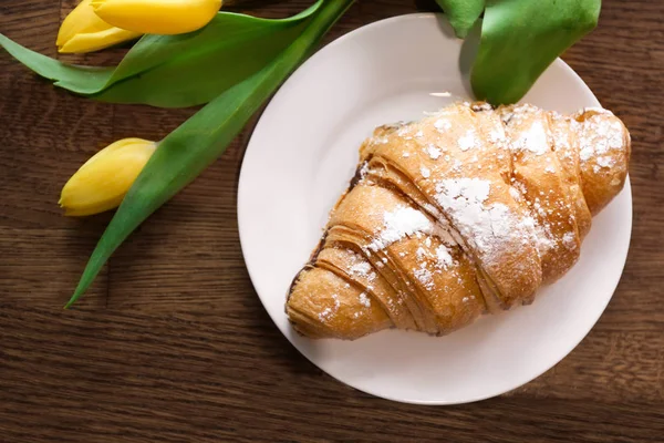 Deska s croissantem a květiny na stole, pohled shora. Chutná snídaně — Stock fotografie