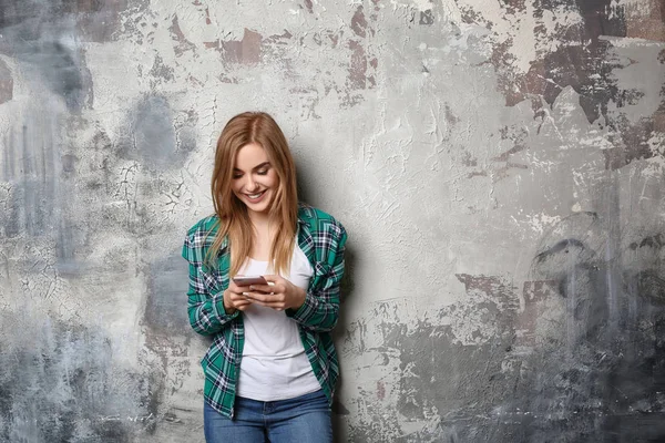Schöne junge Frau mit Handy auf Grunge-Hintergrund — Stockfoto