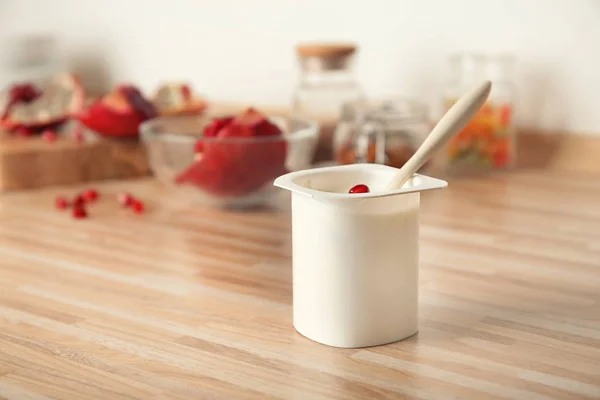 Copa de plástico de yogur delicioso con semillas de granada en la mesa de madera — Foto de Stock