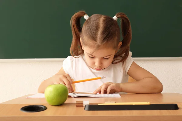 Милая маленькая девочка делает домашнее задание в классе — стоковое фото