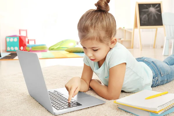Menina bonito usando laptop enquanto fazendo lição de casa dentro de casa — Fotografia de Stock