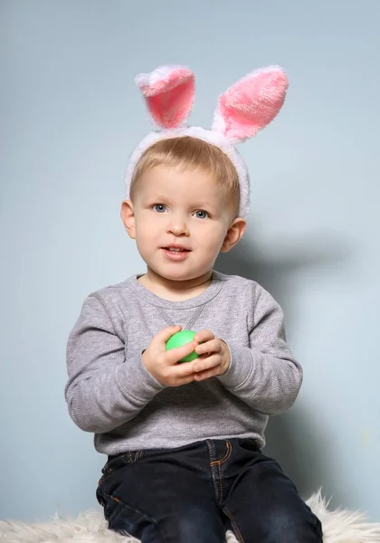 Χαριτωμένο μικρό αγόρι με τα αυτιά λαγουδάκι, κρατώντας το αυγό του Πάσχα σε γκρίζο φόντο — Φωτογραφία Αρχείου