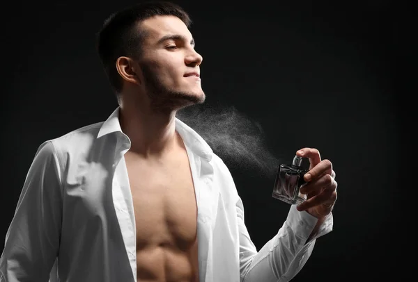 Bello uomo in camicia sbottonata e con bottiglia di profumo su sfondo scuro — Foto Stock