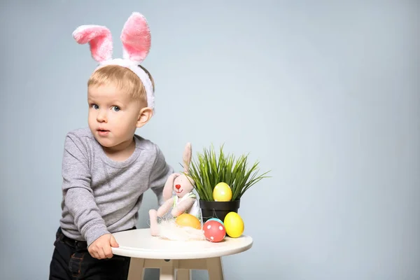 Lindo niño pequeño con orejas de conejo y huevos de Pascua sobre fondo gris — Foto de Stock