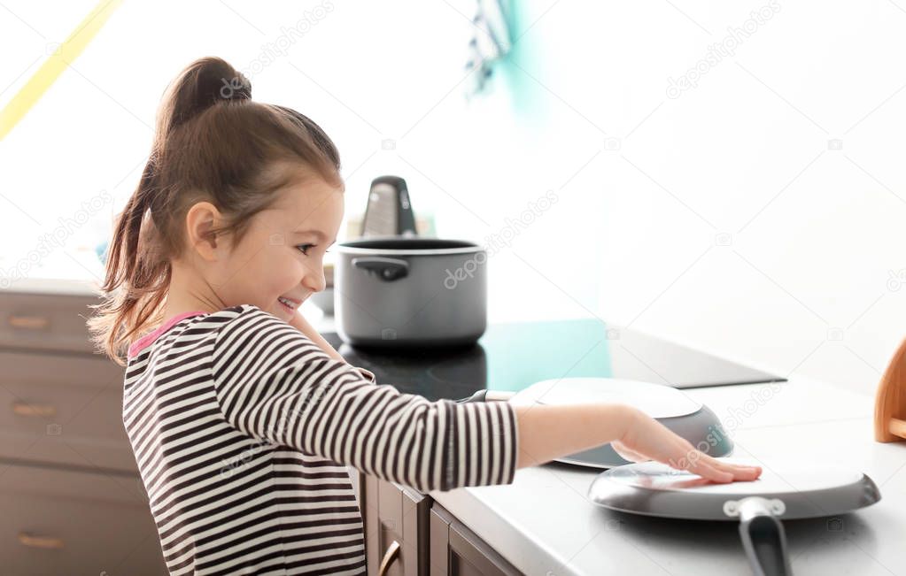 Cute little girl imagining herself DJ while playing with frying pan in kitchen