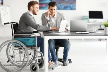 Young man in wheelchair with colleague at workplace