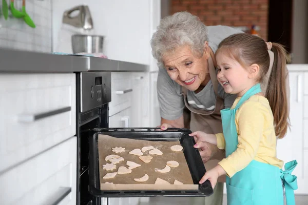 可爱的小女孩和她的祖母做厨房里的饼干 — 图库照片