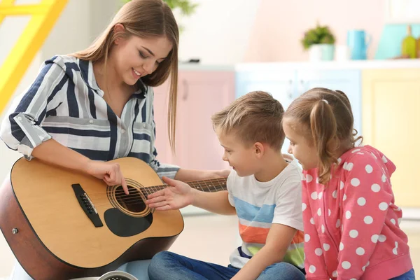 Mother playing guitar for her little children at home