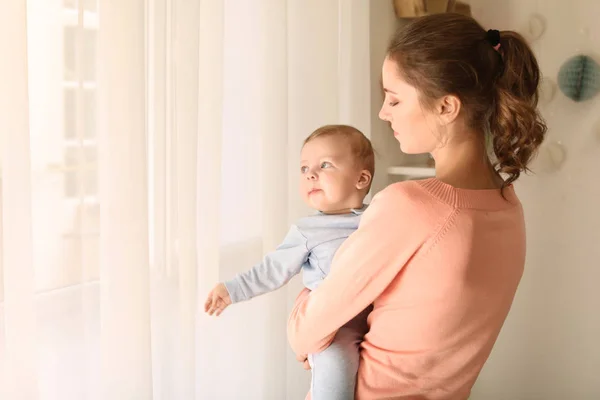 Giovane madre con il suo piccolo bambino carino vicino alla finestra a casa — Foto Stock