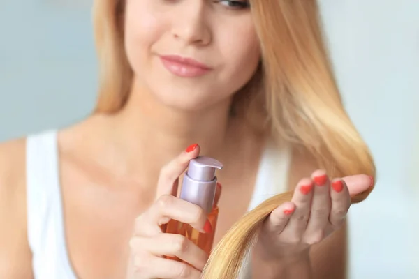 Young woman applying oil onto her hair, indoors — Stock Photo, Image