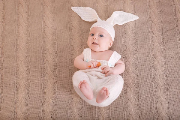 Bebê bonito em traje de coelho com cenoura deitada em xadrez, vista superior — Fotografia de Stock