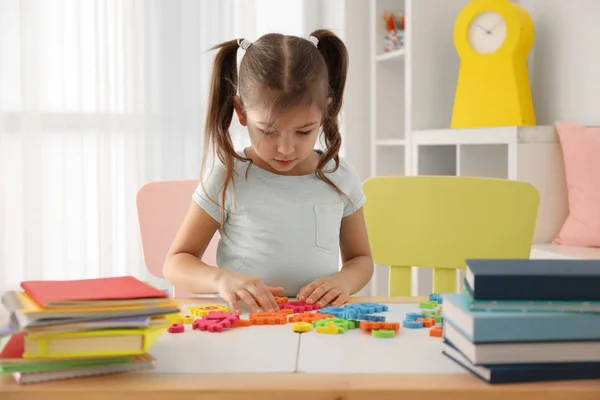 Cute little girl playing with figures while doing homework indoors — Stock Photo, Image