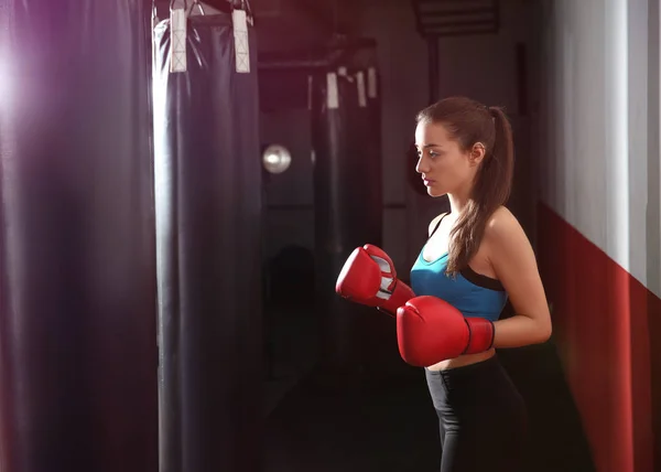 Young female boxer training with punching bag in gym