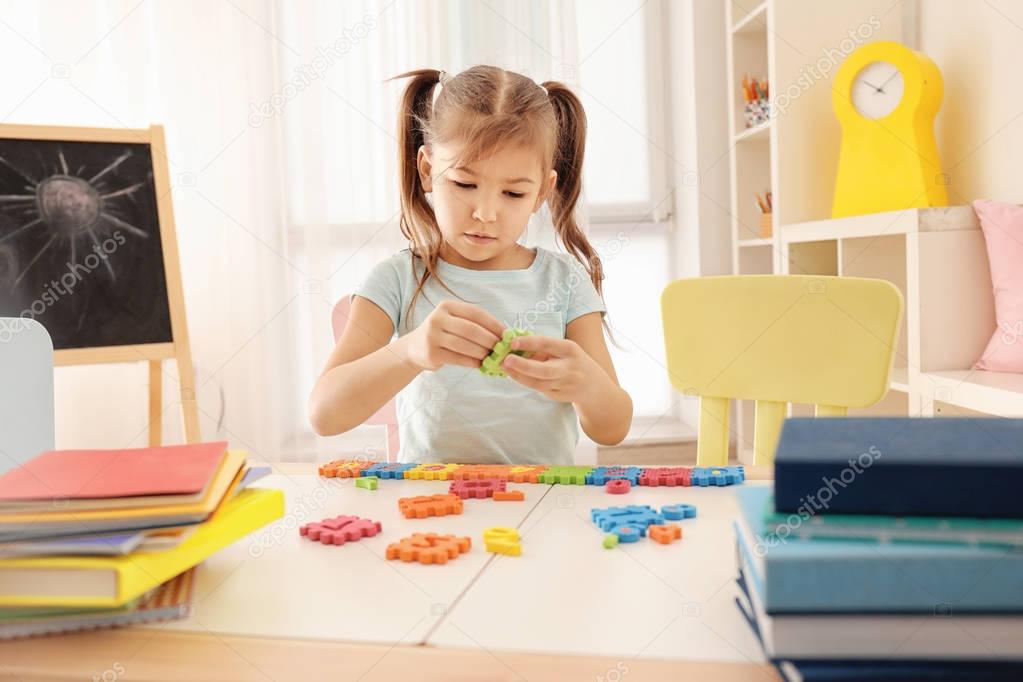 Cute little girl playing with figures while doing homework indoors