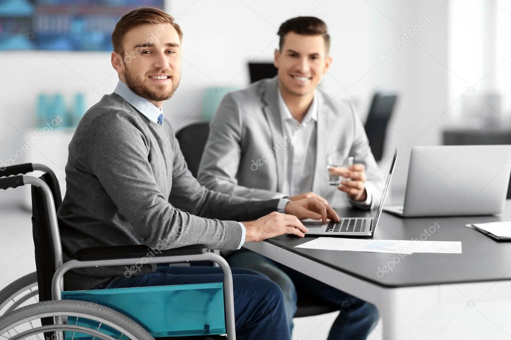 Young man in wheelchair with colleague at workplace