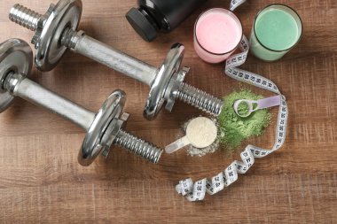 Composition with different protein powders, shakes and dumbbells on wooden background clipart