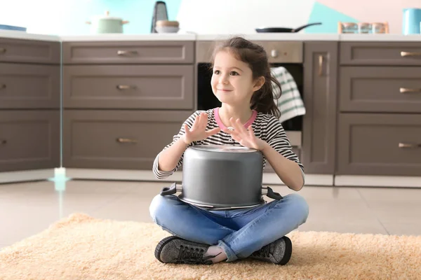 Милая маленькая девочка играет с кастрюлей, как барабан в помещении — стоковое фото
