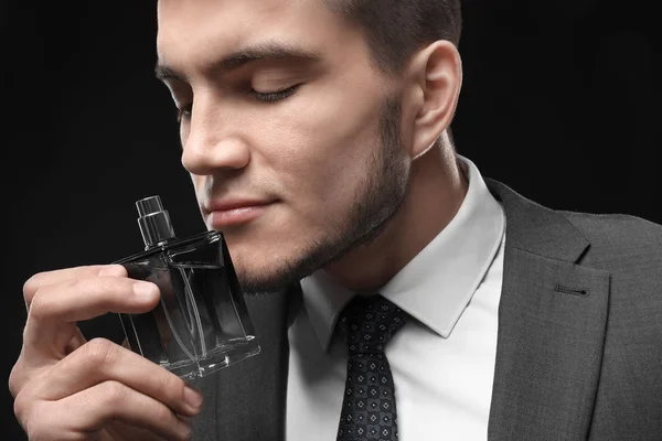 Handsome man in formal suit and with bottle of perfume on dark background, closeup — Stock Photo, Image