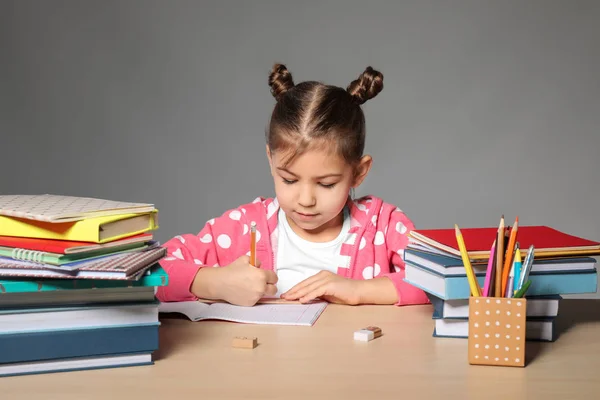 Roztomilá holčička dělat domácí úkoly šedé pozadí — Stock fotografie