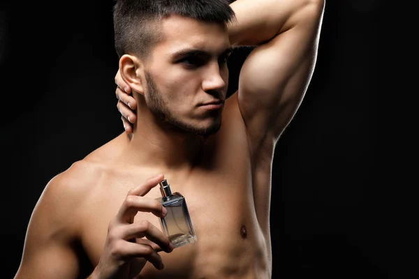 Handsome man with bottle of perfume on dark background — Stock Photo, Image