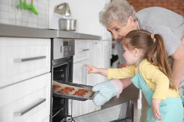 可爱的小女孩和她的祖母从烤箱在厨房拿出曲奇饼 — 图库照片