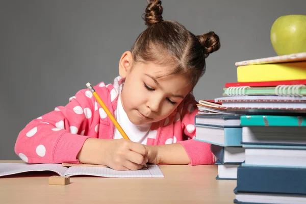 Милая маленькая девочка делает домашнее задание на сером фоне — стоковое фото