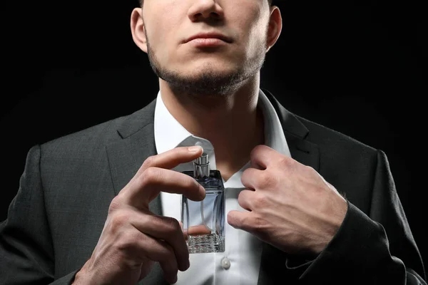 Handsome man in formal suit and with bottle of perfume on dark background, closeup — Stock Photo, Image