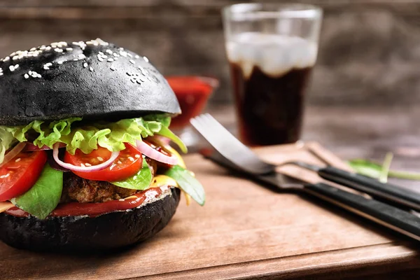 Hambúrguer saboroso com pão preto na placa de madeira, close-up — Fotografia de Stock