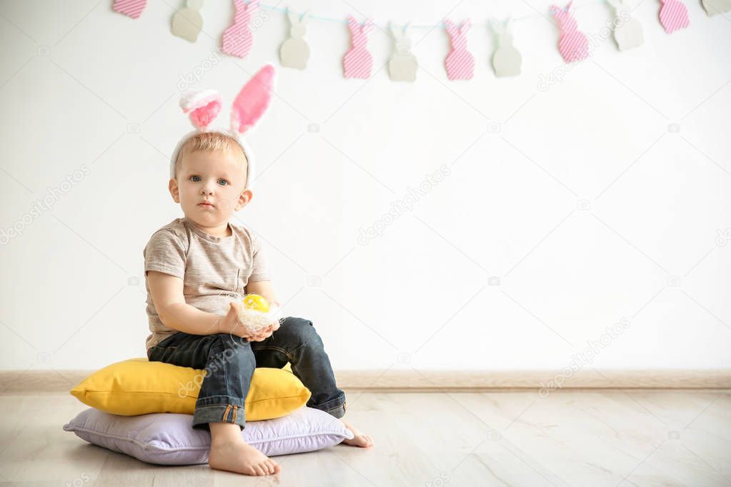 Cute little boy with bunny ears holding Easter egg indoors