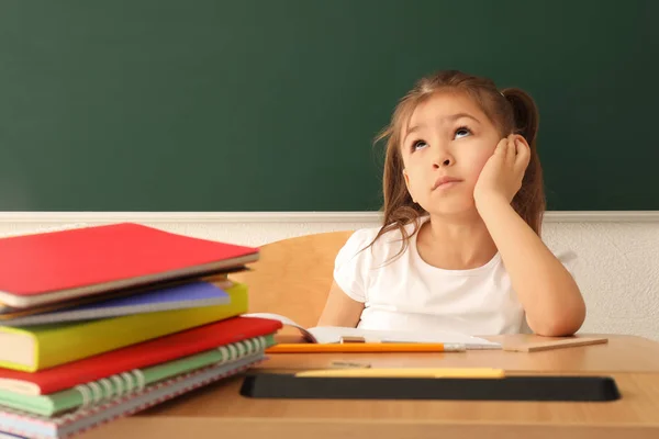 Thoughtful little girl doing homework in classroom — Stock Photo, Image