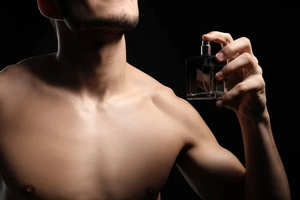 Handsome man with bottle of perfume on dark background, closeup — Stock Photo, Image