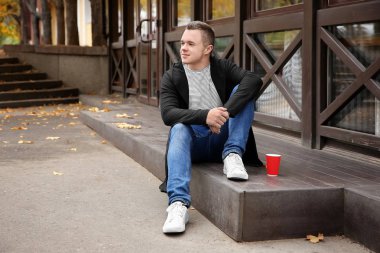 Hipster genç açık havada kapının eşiğine oturup kahve ile