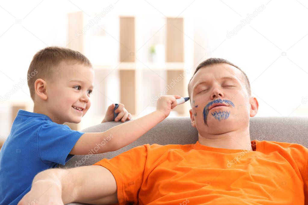 Little boy painting his father's face while he sleeping. April fool's day prank