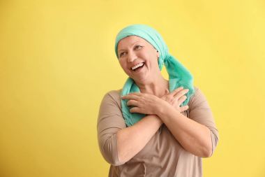 Mature woman with cancer in headscarf on color background clipart