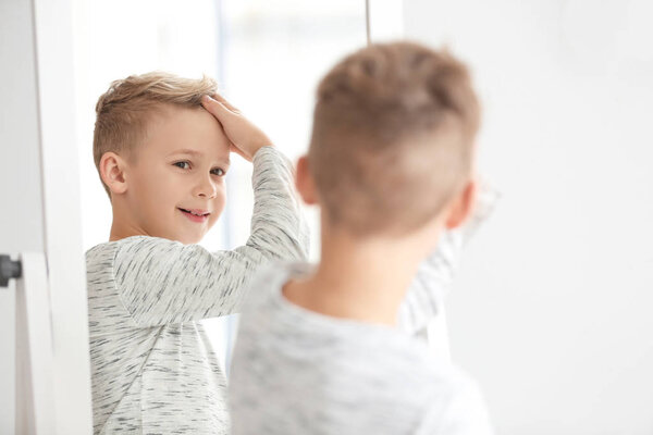 Cute little boy looking at himself in mirror indoors