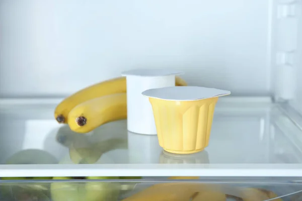 Copos de plástico com iogurte e bananas na geladeira — Fotografia de Stock