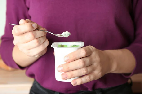 Woman eating yogurt with pieces of kiwi indoors, closeup — Stock Photo, Image