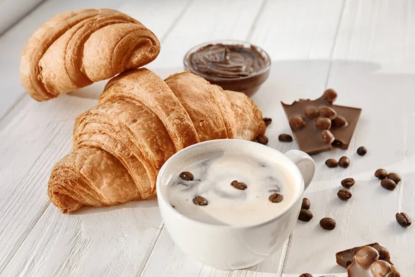 Csésze kávé és csokoládé szósszal, a fából készült asztal, ízletes croissant — Stock Fotó